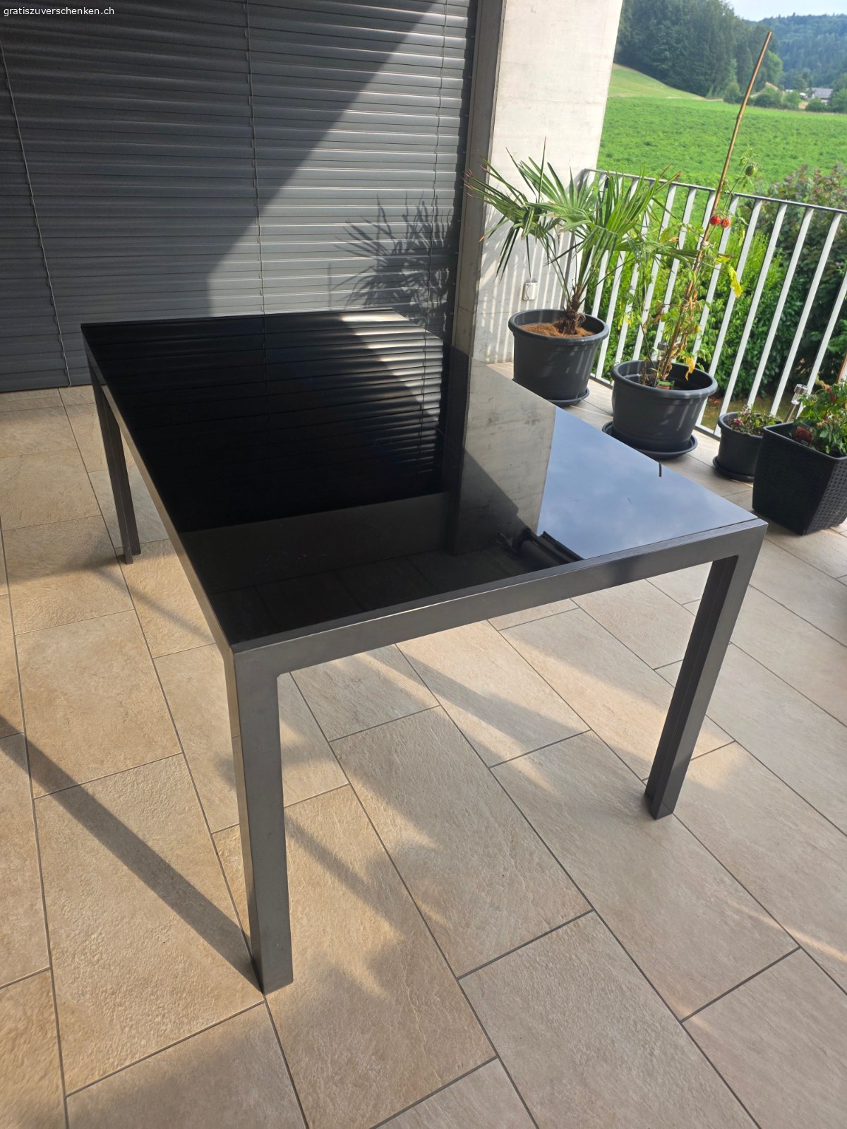 Glastisch Balkon. Der Tisch ist gebraucht und in funktionstüchtigem Zustand. Er hat sichtbare Kratzer auf der Tischplatte. Die Masse betragen 150 cm (Länge/Tiefe) x 90 cm (Breite) x 71 cm (Höhe). Es handelt sich um einen Balkontisch in schwarzer Farbe.